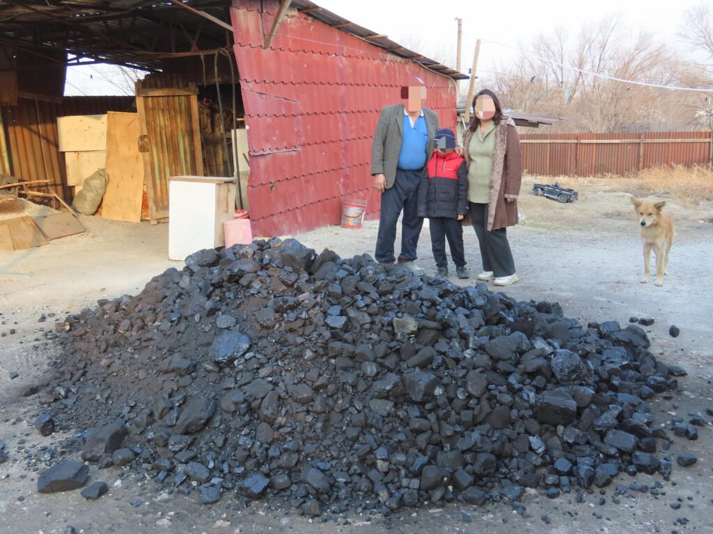 Family of three standing behind a large pile of coal.